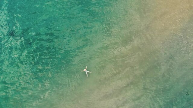 Aerial view of young woman swimming in the transparent turquoise sea water