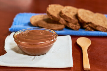 Dulce de leche in glass container, on wooden table, with wholemeal bread on the side, Cajeta. Argentine food concept.