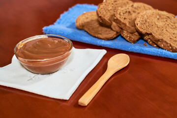 Dulce de leche in glass container, on wooden table, with wholemeal bread on the side, Cajeta. Argentine food concept.