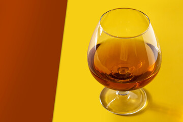 Cognac or whiskey drink on yellow and brown background. Copy space