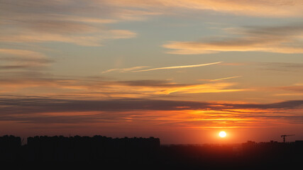 Beautiful dramatic sunset background. Orange sky with sun, clouds and black silhouettes of urban buildings