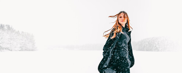 portrait of young teenage girl with long hair in black coat on natural snow background in field....