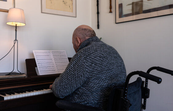 Elderly Man Disabled Pensioner Playing The Piano Or Synthesizer. Portrait Of Senior Aged Musician. Rehabilitation Of Disabled People Through Creativity. A Person In Wheelchair.