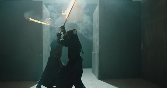 Japanese kendo fighters with burning swords competing in the fog in dark mystic industrial building . Super mystical video . Battle of two kendo fighter with fire sword . Shot on ARRI Alexa Camera .