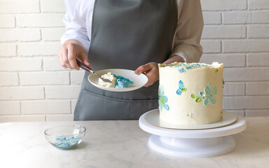 Female baker decorating with cream tasty cake on the table