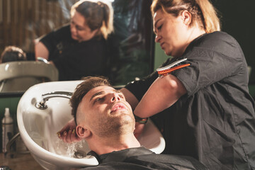 Hairdressing, girl hairdresser washes the head of a young guy in a barbershop