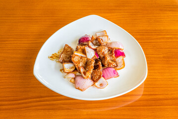 Plate of beef with wok-sautéed onions with yakitori sauce on cherry-colored table