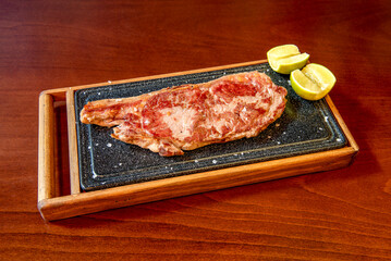 great beef entrecote served on the same hot plate with wood protection with sea salt flakes and lemon wedges