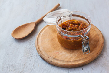 Open jar of chutney on a round cutting board on a gray table.