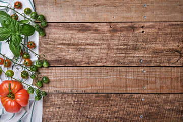 Fresh cherry tomato branches, basil leaves, napkin, pepper and pepper mill on old wooden rustic background. Food cooking background and mock up.