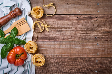 Pasta tagliatelle, spices, basil and fresh tomatoes on old wooden rustic background table. Food cooking and pasta background. Top view with copy space.