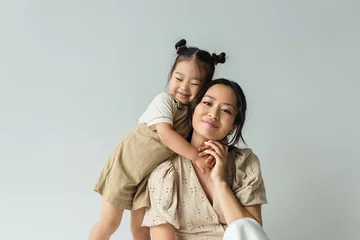 Foto op Plexiglas cheerful asian toddler daughter hugging happy mother isolated on gray © LIGHTFIELD STUDIOS