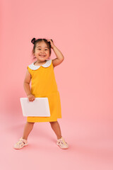 full length of happy asian toddler kid in yellow dress holding digital tablet on pink