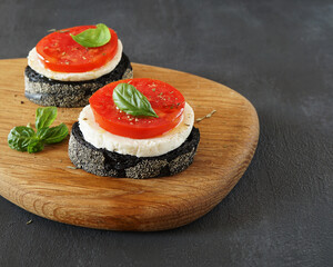  two sandwiches  with black ciabatta, Adyghe cheese and tomato lies on a wooden board in the left  and basil  . place for text