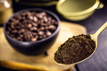 golden metal spoon with ground coffee. Roasted seeds in blurred background and copyspace