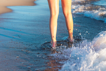 Woman legs and feet walking on sand of the beach with the sea water in the backgroundWalking on the beach sea side.