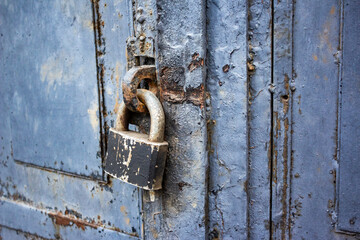 A blue old wooden door with a rusty steel lock. Farm gate from planks with an old padlock. The lock on the door of the shed. Reliable old barn rusty padlock on a wooden door 
