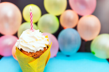 Birthday cupcake.Pastel yellow birthday cupcake with candle and blurred balloons.colorful birthday.Closeup,copy space.