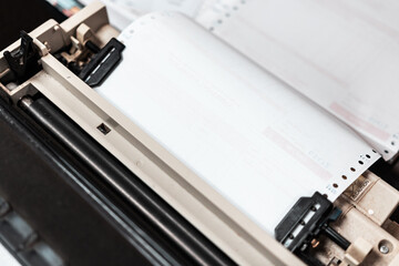 Close up of continuous paper being feed into old dot matrix printer. Dot matrix printer can print multiple (copy) of document or receipt at once.