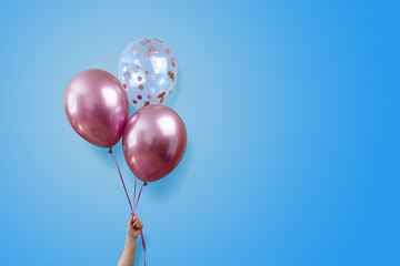 stylish birthday party or holidays with balloons close up. Hand  holding three pink balloons isolated on blue background with copy space for text. background for birthday greeting card or other event