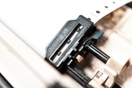 Close up of continuous paper being feed into old dot matrix printer. Dot matrix printer can print multiple (copy) of document or receipt at once.