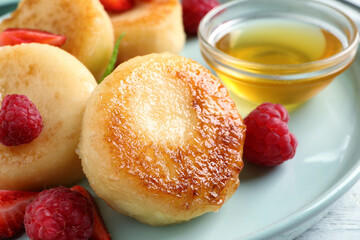 Delicious cottage cheese pancakes with fresh berries and honey on plate, closeup