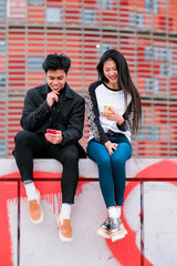 Happy young asian couple using smartphone on city street