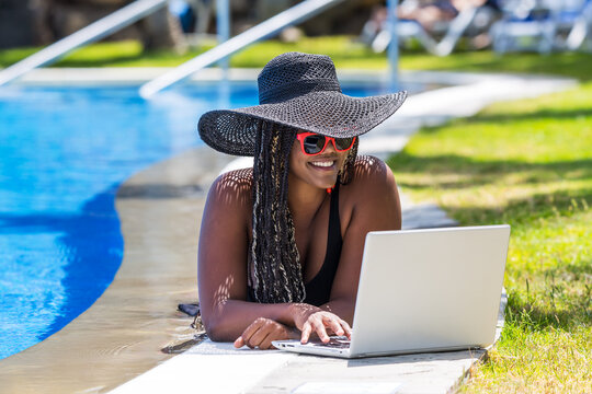 Woman lying on the edge of the pool with a laptop - Powered by Adobe