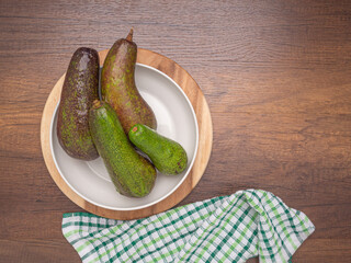 Flat lay of ripe avocados on a white dish on a wooden cutting board with cloth on a wooden table. Top view. Flat lay, space for text. Healthy fruits concept