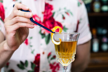 Bartender decorating glass of fresh alcoholic cocktail on bar counter, close-up