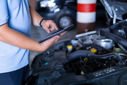 Auto mechanic with digital tablet at work making an engine repair diagnosis of a car in a mechanic garage
