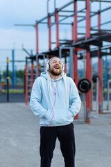 A man with a braid hairstyle in the early morning listens to music on headphones on the sports field and laughs