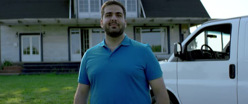 Portrait of Hispanic male handyman general worker posing near the house . White car with copy space. Shot with 2x anamorphic lens