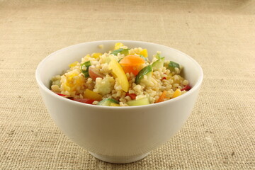 Freshly made Bulgur salad with colourful fruit and vegetables in a white bowl on a hessian background