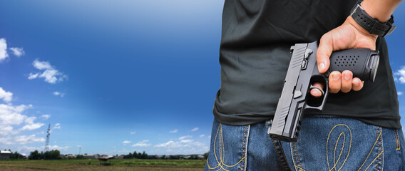Male holds automatic 9mm black pistol, blurred bluesky background, concept for protecting crops, security, bodyguard, gangster, killer, murder, robber and shooting sport around the word.