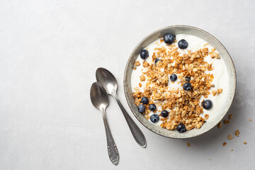 Yogurt with granola and blueberries in bowl on concrete background