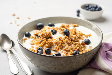 Yogurt with granola and blueberries in bowl on concrete background