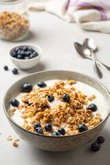 Yogurt with granola and blueberries in bowl on concrete background