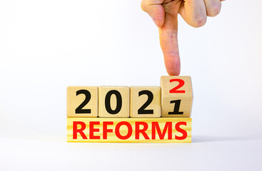 Symbol of planning 2022 reforms new year. Businessman turns a wooden cube and changes words...
