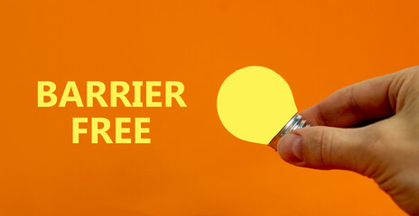 Barrier free symbol. Businessman holds yellow shining light bulb. Words 'Barrier free', beautiful orange background. Business, diversity, inclusion, belonging and barrier free concept. Copy space.