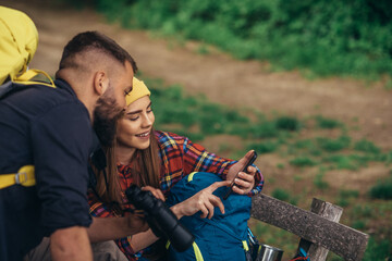 Hikers taking a break while sitting on the bench in the forest and using smartphone