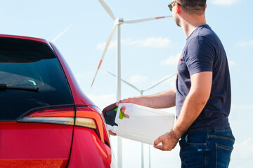 Man filling a diesel engine fluid from canister into the tank of red car on the background of wind...
