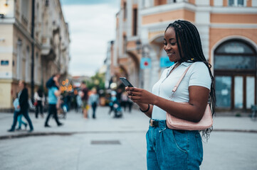 Cheerful african american woman using a smartphone while out in the city