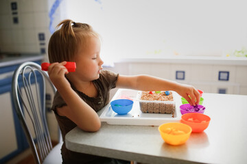 Montessori and Sensory Development, A child in the kitchen learns colors, sorts toy figures by color. The child is playing with tweezers,