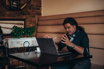 Senior Hispanic cuban man having an online meeting while using a laptop and sitting in a cafe