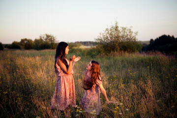 Two sisters dance barefoot in a field at sunset.