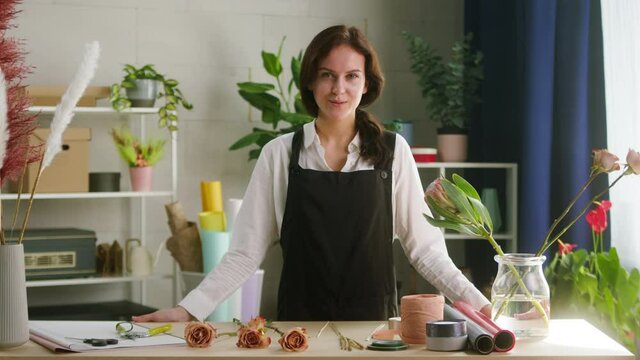 Portrait of young woman florist standing near workplace and smiling. Floral artist working in flower shop. Floristry is prepared for masterclass on making a bouquet of dried flowers. Small business.