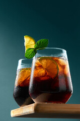 Cuba Libre or Long Island Cocktail with rum, cola and lime in glasses on wooden board on dark blue background. Refreshing summer drink