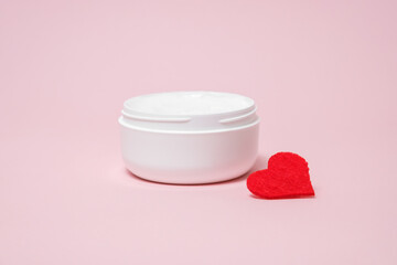 A jar of thick cream and a heart on a pink background