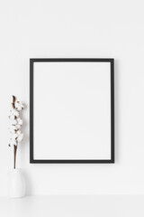 Black frame mockup on the wall with a  cotton branch decoration.